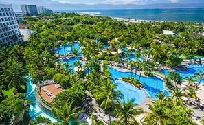 Un complexe hôtelier doté de plusieurs piscines, entouré d’une végétation luxuriante et de palmiers, et offrant une vue sur une plage et l’océan.