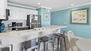 Une cuisine avec des meubles blancs, un plan de travail en marbre, un réfrigérateur et un tableau accroché au mur.