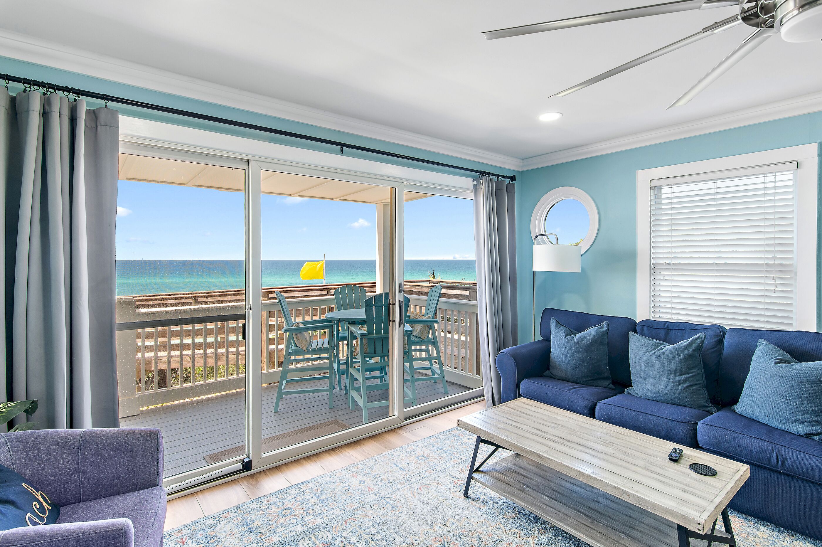 A living room with a view of the ocean, a ceiling fan, and a blue sofa.