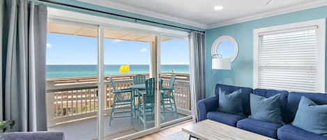 A living room with a view of the ocean, a ceiling fan, and a blue sofa.