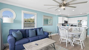 Un salon avec un canapé bleu, une table basse en bois et un coin repas avec des chaises blanches.