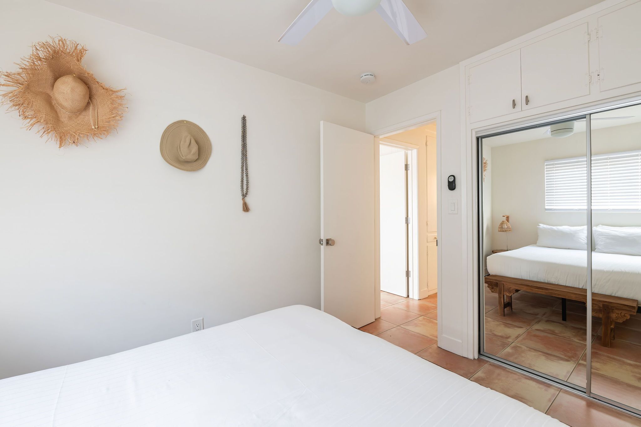 A bedroom with a bed, a wardrobe, a ceiling fan, and a door leading to another room.