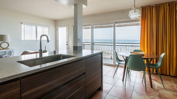 Une cuisine moderne dotée d’un grand îlot central, d’un coin repas avec des chaises et offrant une vue sur la mer grâce à de grandes fenêtres.