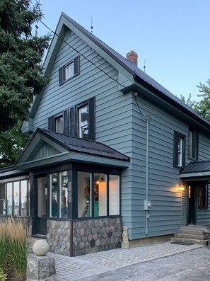 A two-story house with a gabled roof, a stone wall with a decorative pattern, and a small porch with a stone ball.