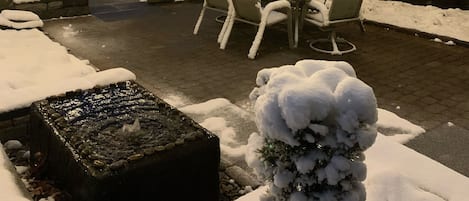 Un patio al aire libre con una mesa y sillas, rodeado de plantas cubiertas de nieve y una valla de madera.