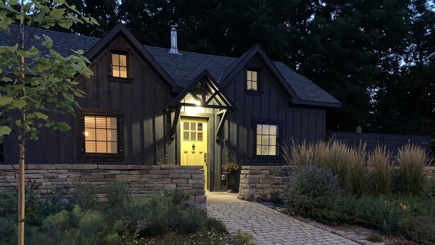 A two-story house with a stone foundation, a central entrance with a yellow door, and a brick pathway leading to the door.
