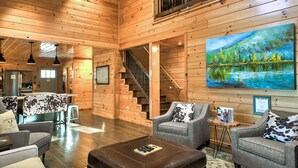 A spacious wooden interior with a staircase, seating area, and a painting of a forest scene. - FishTop Cabin | Luxury Mountain Cabin Across from the Green River (Saluda)