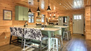A wooden cabin interior with a kitchen, dining area, and bar stools. - FishTop Cabin | Luxury Mountain Cabin Across from the Green River (Saluda)