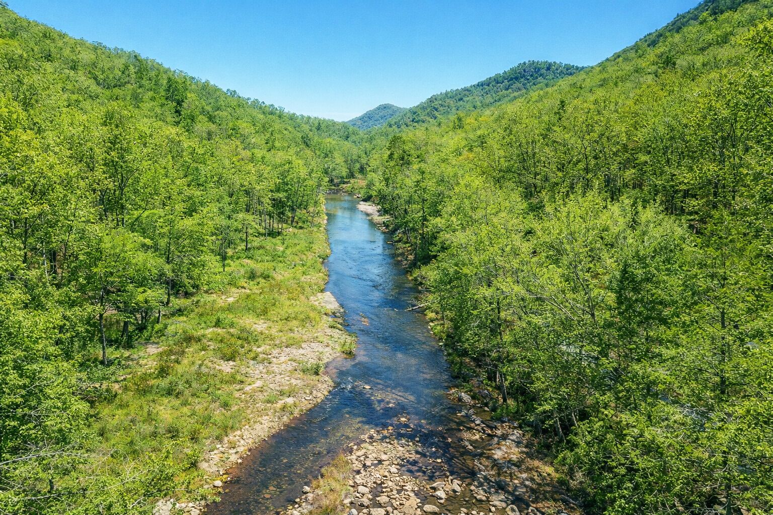 Un fiume che scorre attraverso una valle boscosa, fiancheggiata da colline.