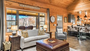 A cozy cabin interior with a living room, dining area, and kitchen. A sign on the wall reads "Life Is Good On The River." - FishTop Cabin | Luxury Mountain Cabin Across from the Green River (Saluda)