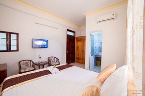 A hotel room with a bed, two chairs, a TV, and an air conditioning unit. - Truong Thinh Homestay (Da Nang)