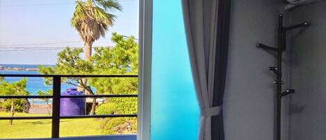 A room with a view of the sea, a balcony with a railing, and a door with a curtain.