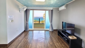 Une chambre dotée d’un plancher en bois, d’un téléviseur à écran plat, d’un ventilateur de plafond et offrant une vue sur la mer depuis une porte-fenêtre donnant sur un balcon.