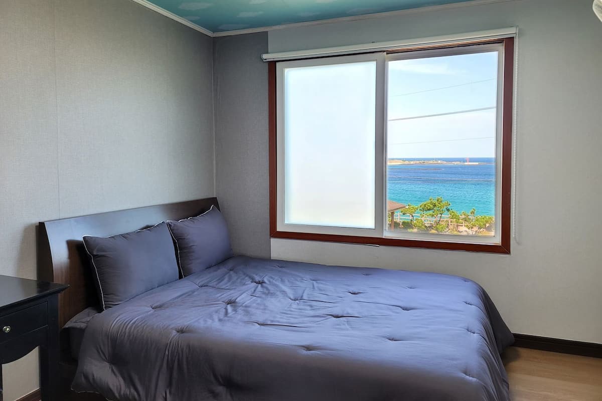 Ein Schlafzimmer mit Bett, Nachttisch und Fenster mit Meerblick.