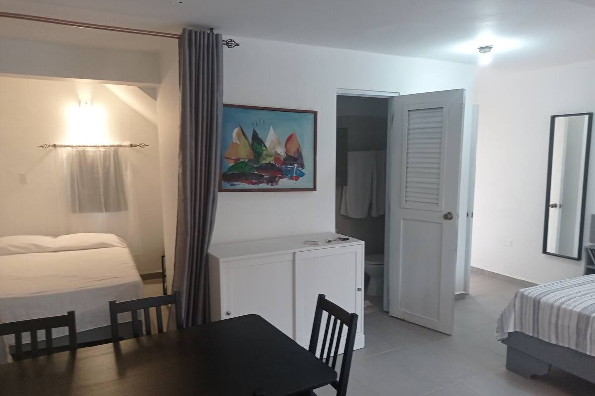 Une chambre d’hôtel comprenant un lit, une table à manger avec des chaises, un tableau, une armoire et une porte donnant sur une autre pièce.