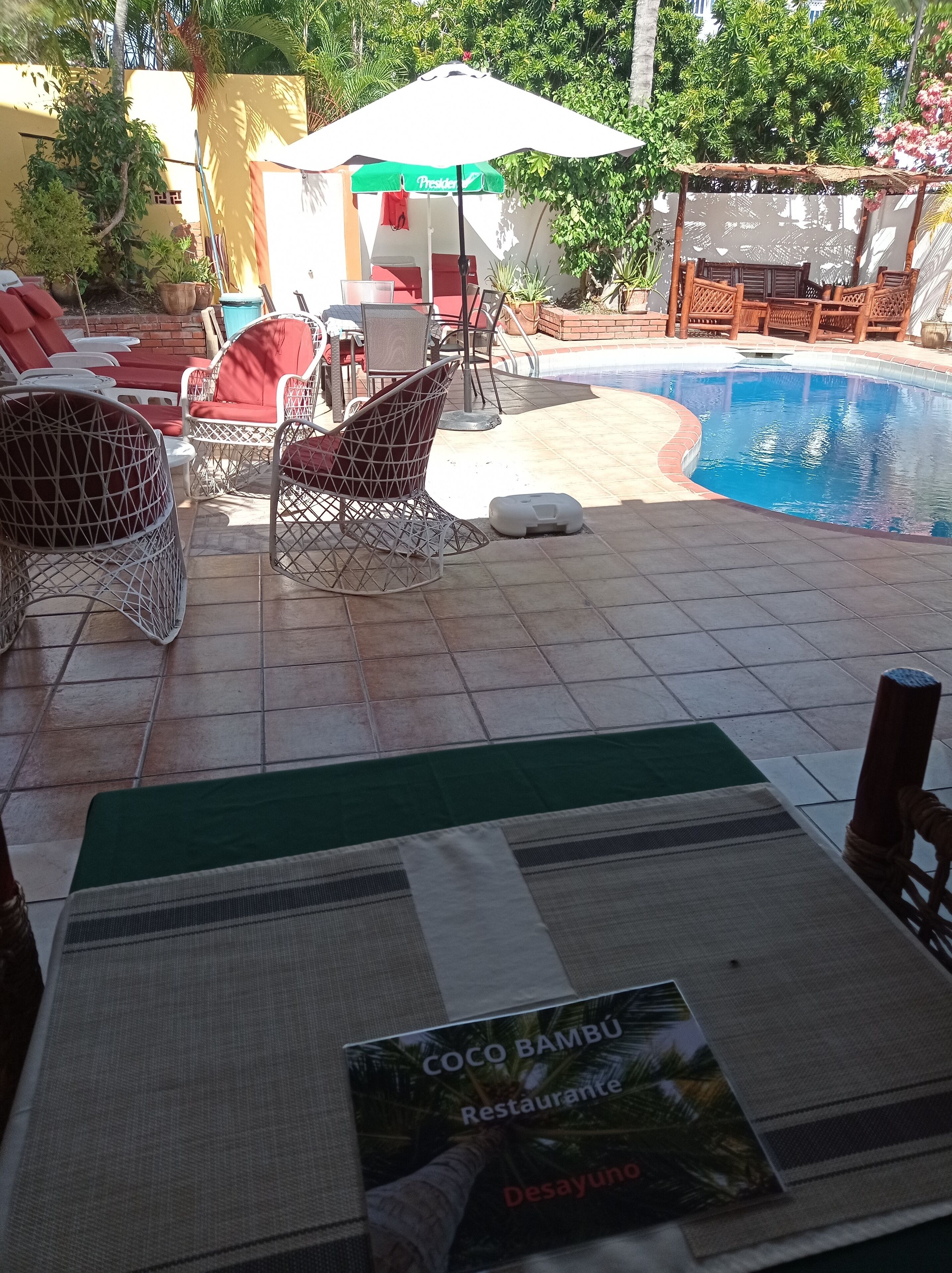 A poolside area with lounge chairs, a table with a placemat, and a sign for 'COCO BAMBU Restaurante'.