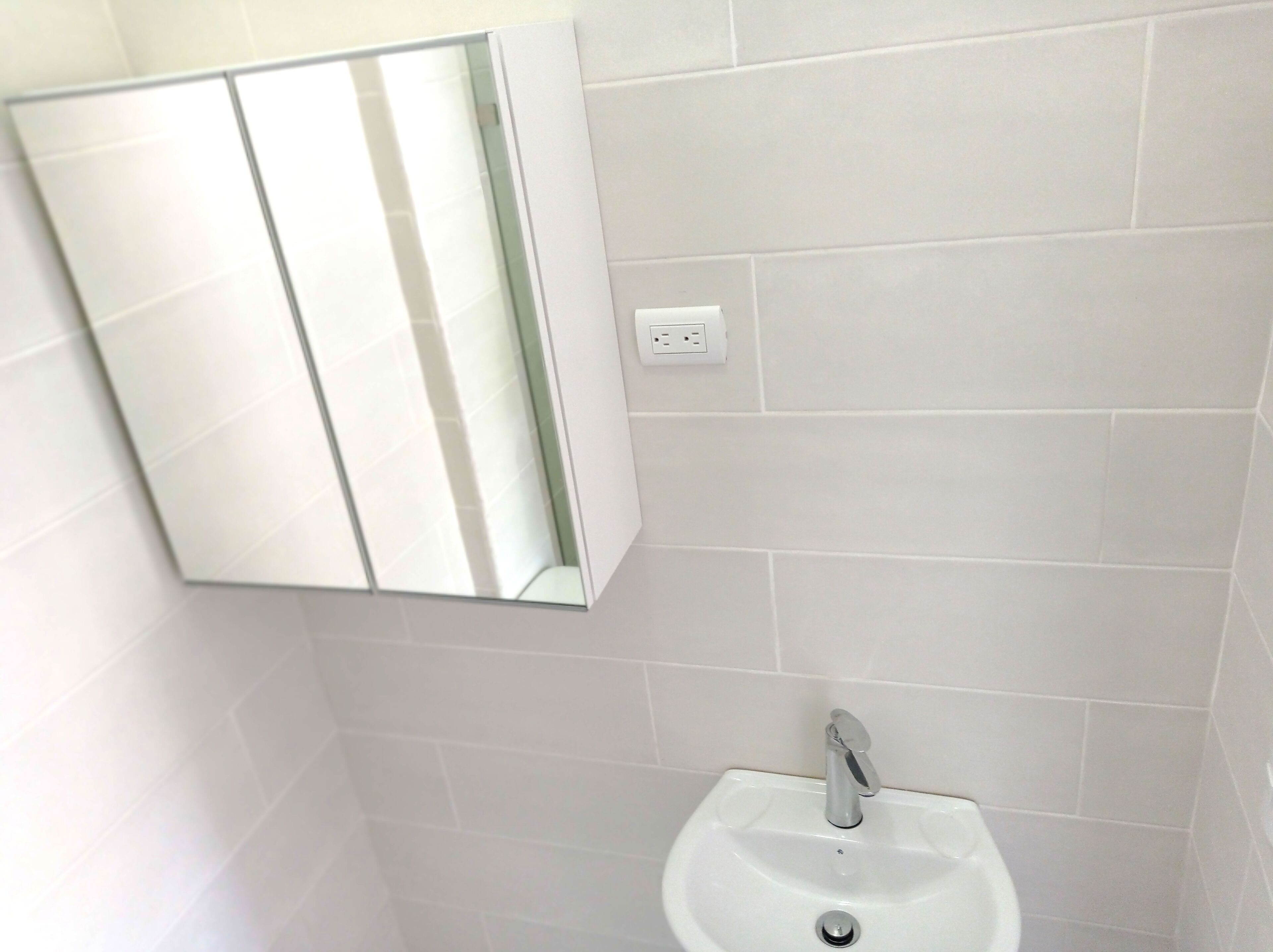 Een badkamer met een wit wastafel, een spiegel en een stopcontact.