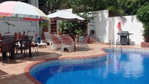 Un área de piscina con solárium de baldosas, mobiliario exterior y sombrillas.