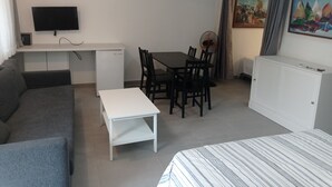 Habitación de hotel compacta con cama, sofá, una mesita, escritorio con televisor, ventilador y un cuadro en la pared.
