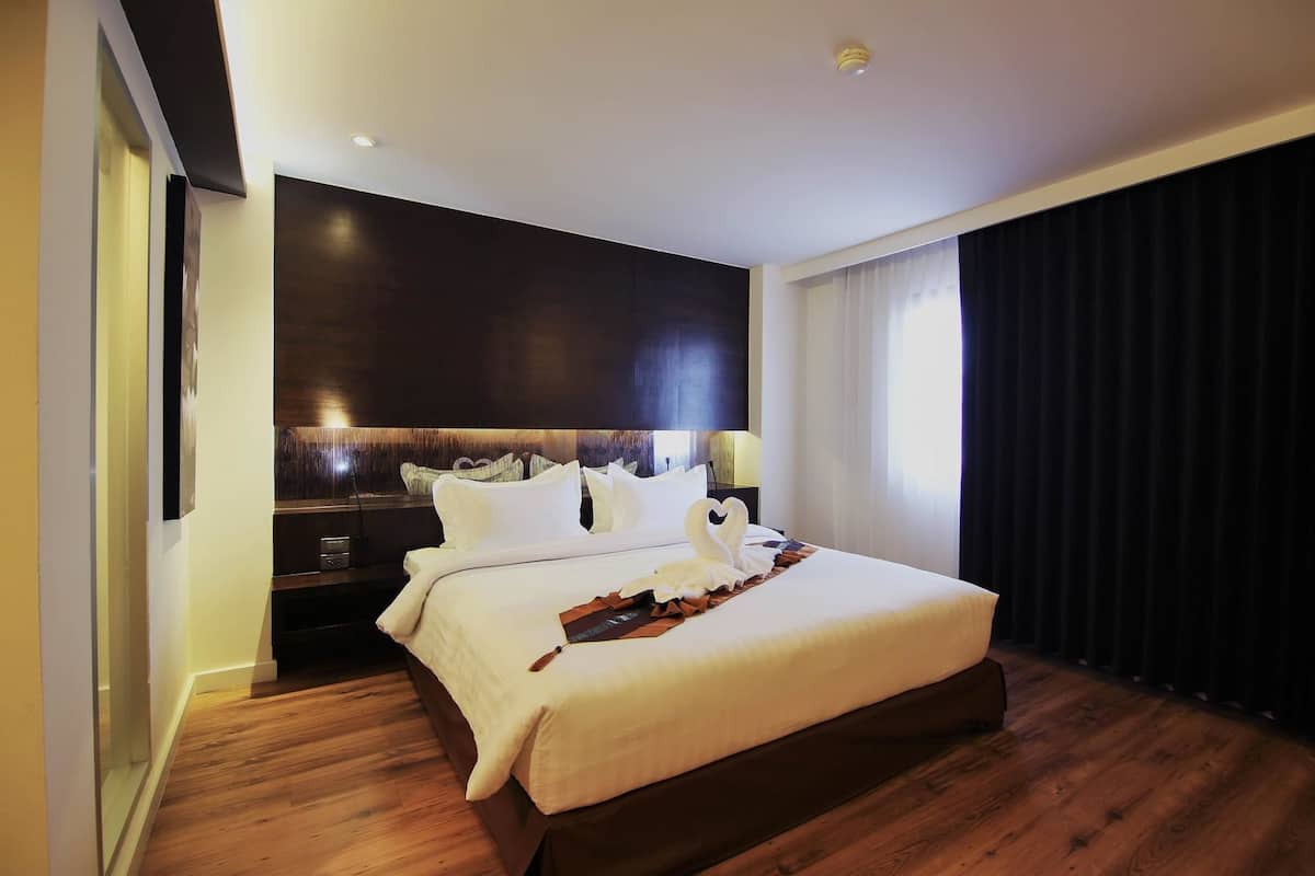 A modern hotel room with a large bed, dark wood flooring, and a dark headboard.