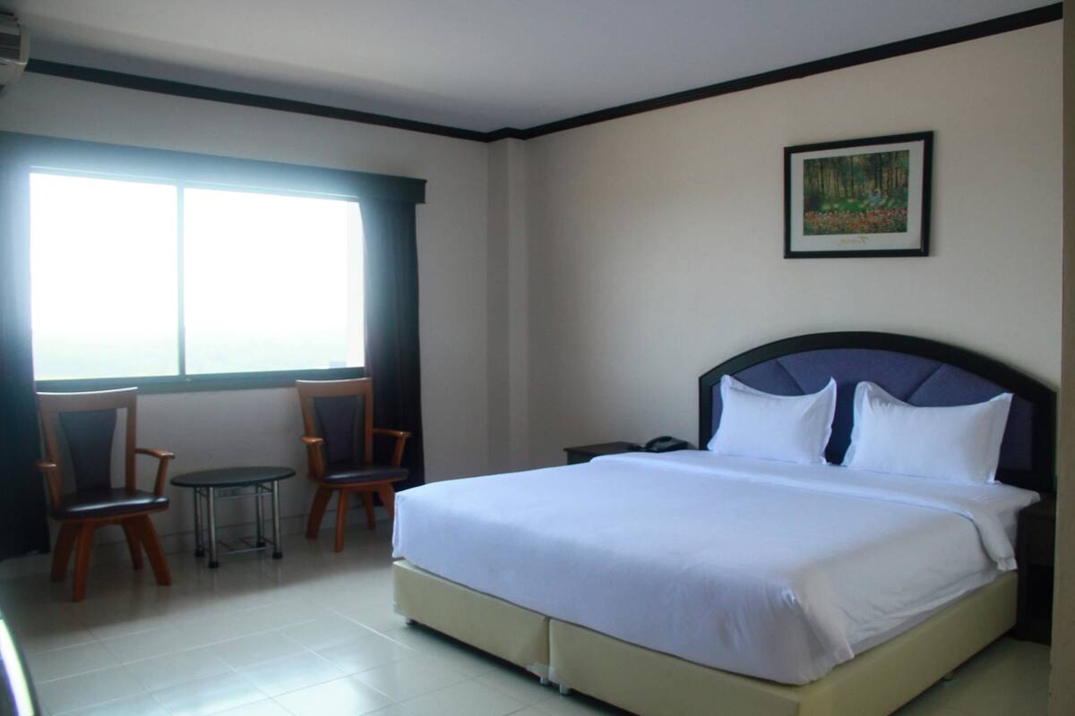 A hotel room with a large bed, two chairs, a small table, and a window with curtains.