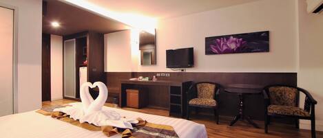 Habitación de hotel con una cama grande, un escritorio, dos sillas, un televisor de pantalla plana y un aire acondicionado instalado en la pared.