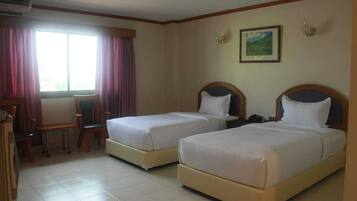 A hotel room with two single beds, a desk, a chair, and a window with curtains.