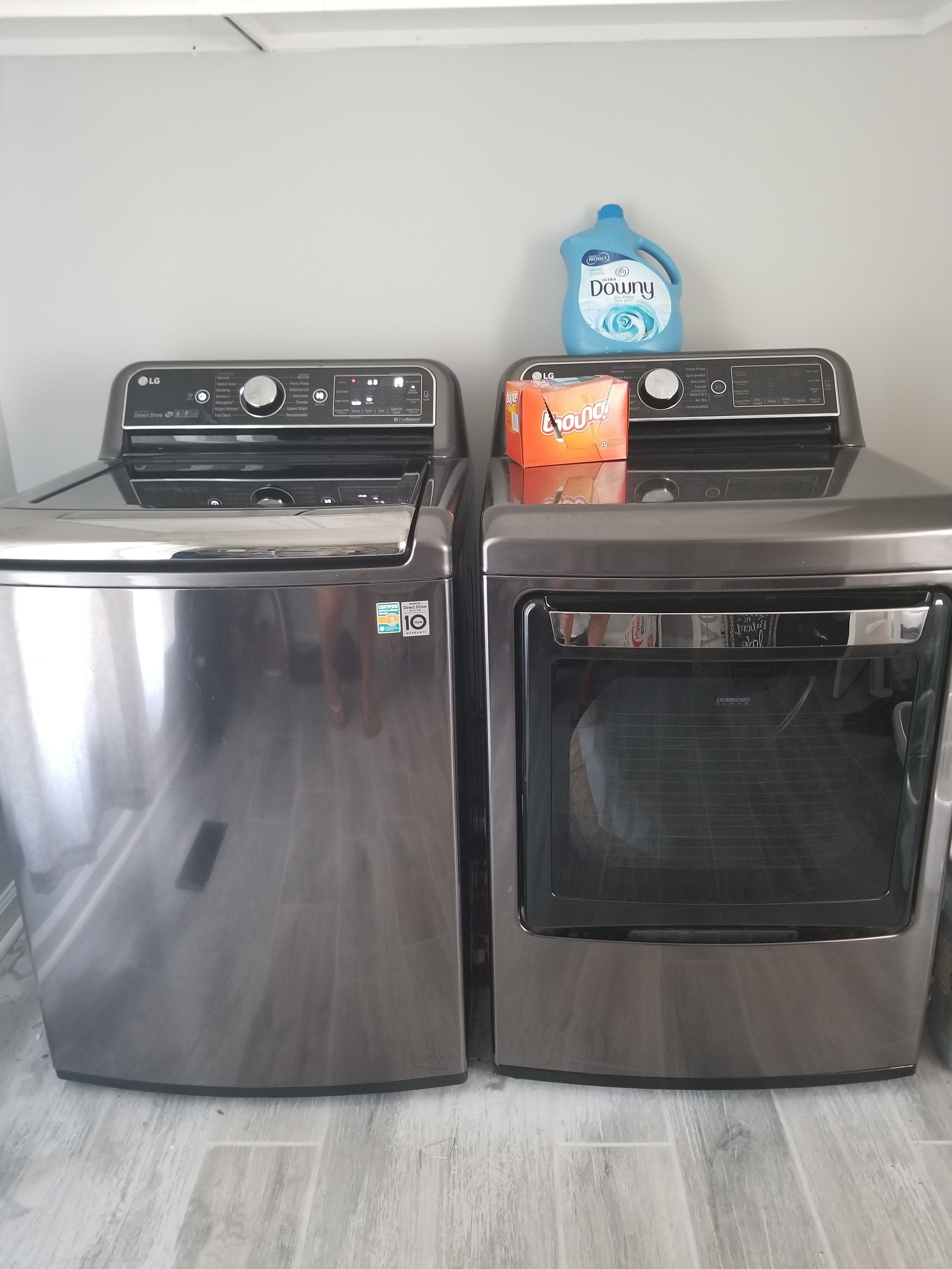 Two stainless steel appliances, a dryer and a dishwasher, with a blue detergent box on top.