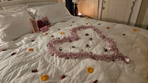 A bed with a heart-shaped tinsel garland and scattered rose petals. - Kernersville Hot Tub  Pool  Arcade Gym Wifi Coffee (Kernersville)