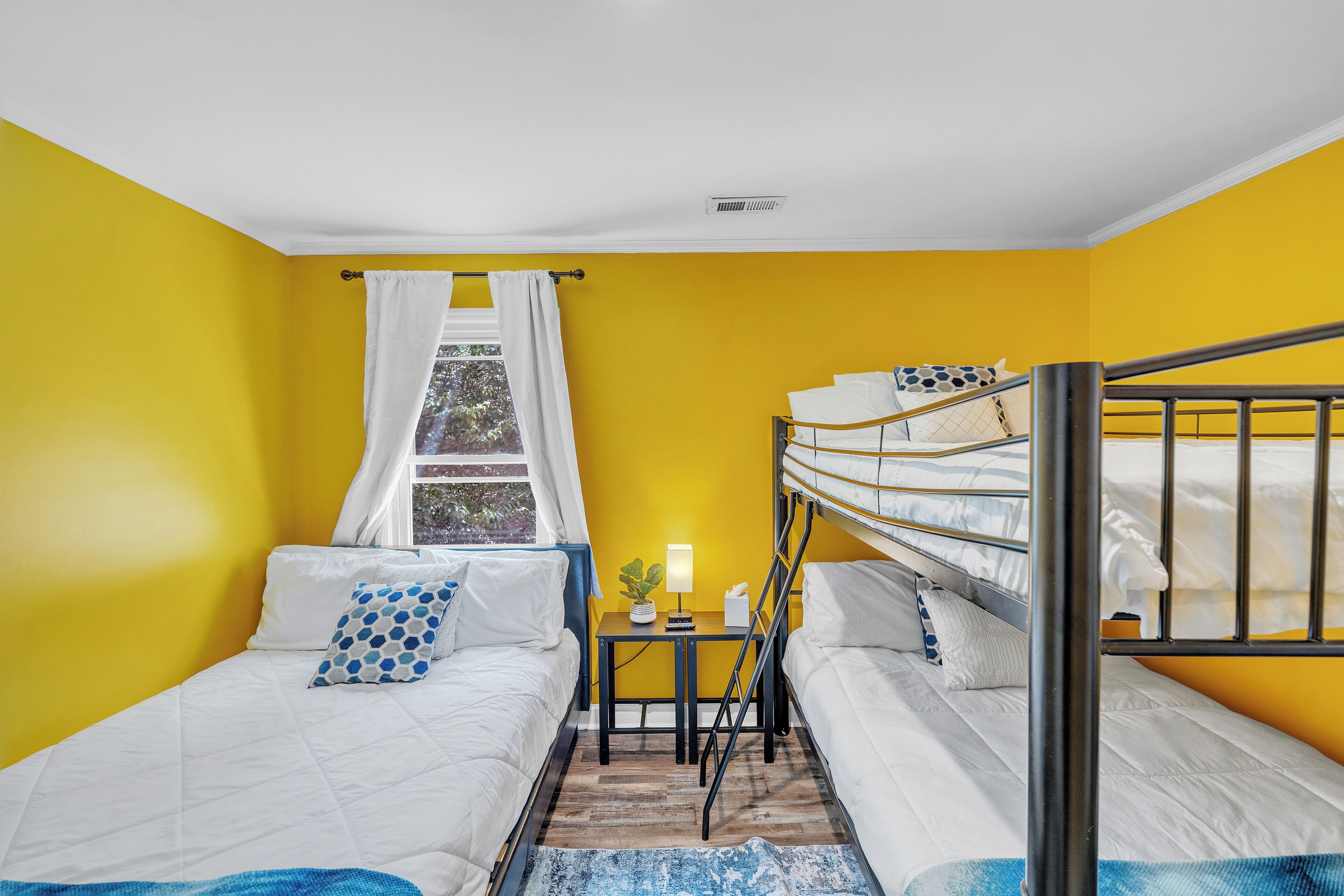 Ein Zimmer mit gelben Wänden, einem Etagenbett, einem Schreibtisch mit Lampe und einem Fenster mit Vorhängen.