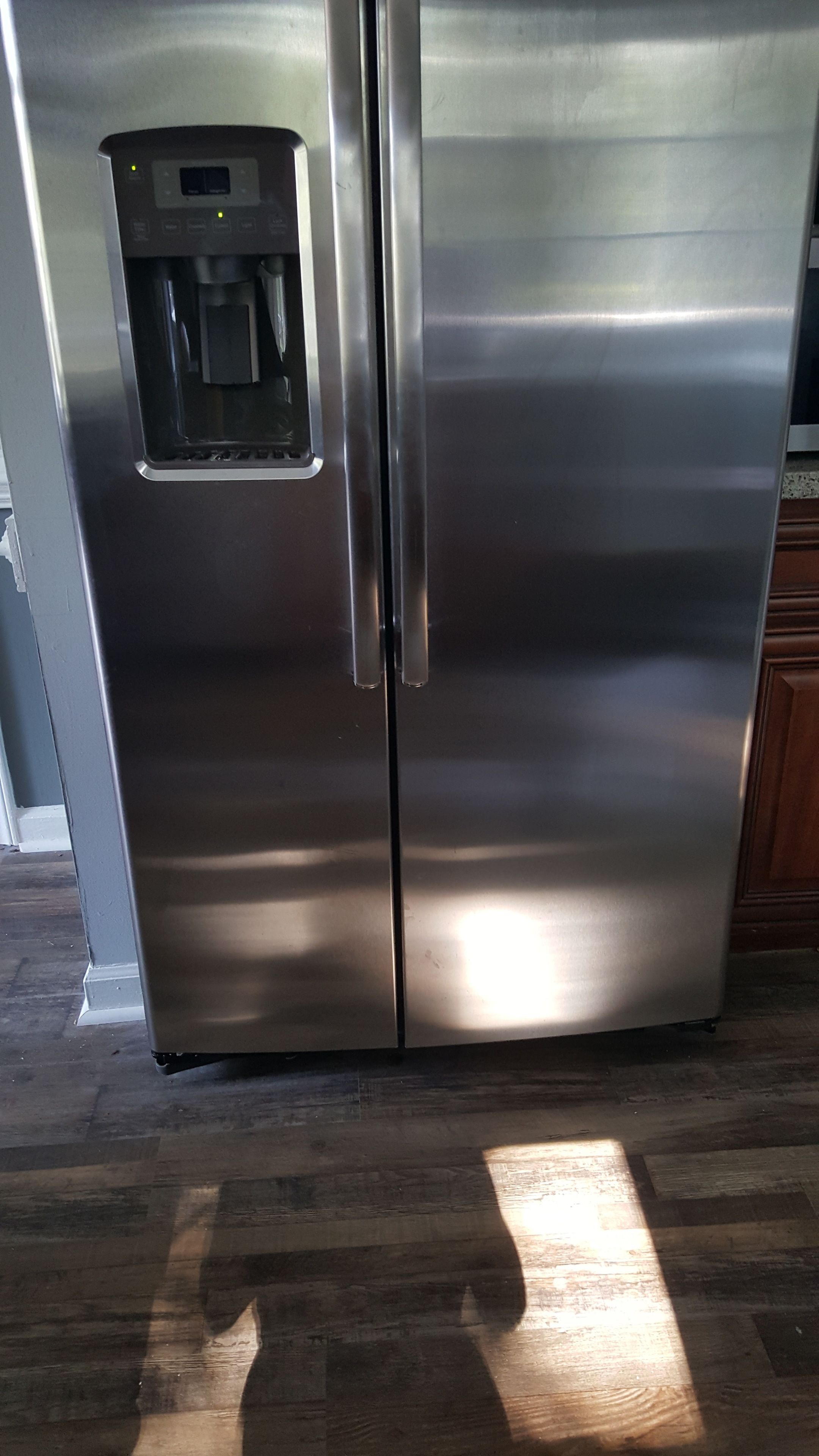 A stainless steel refrigerator with a water dispenser, located in a kitchen with wooden flooring.