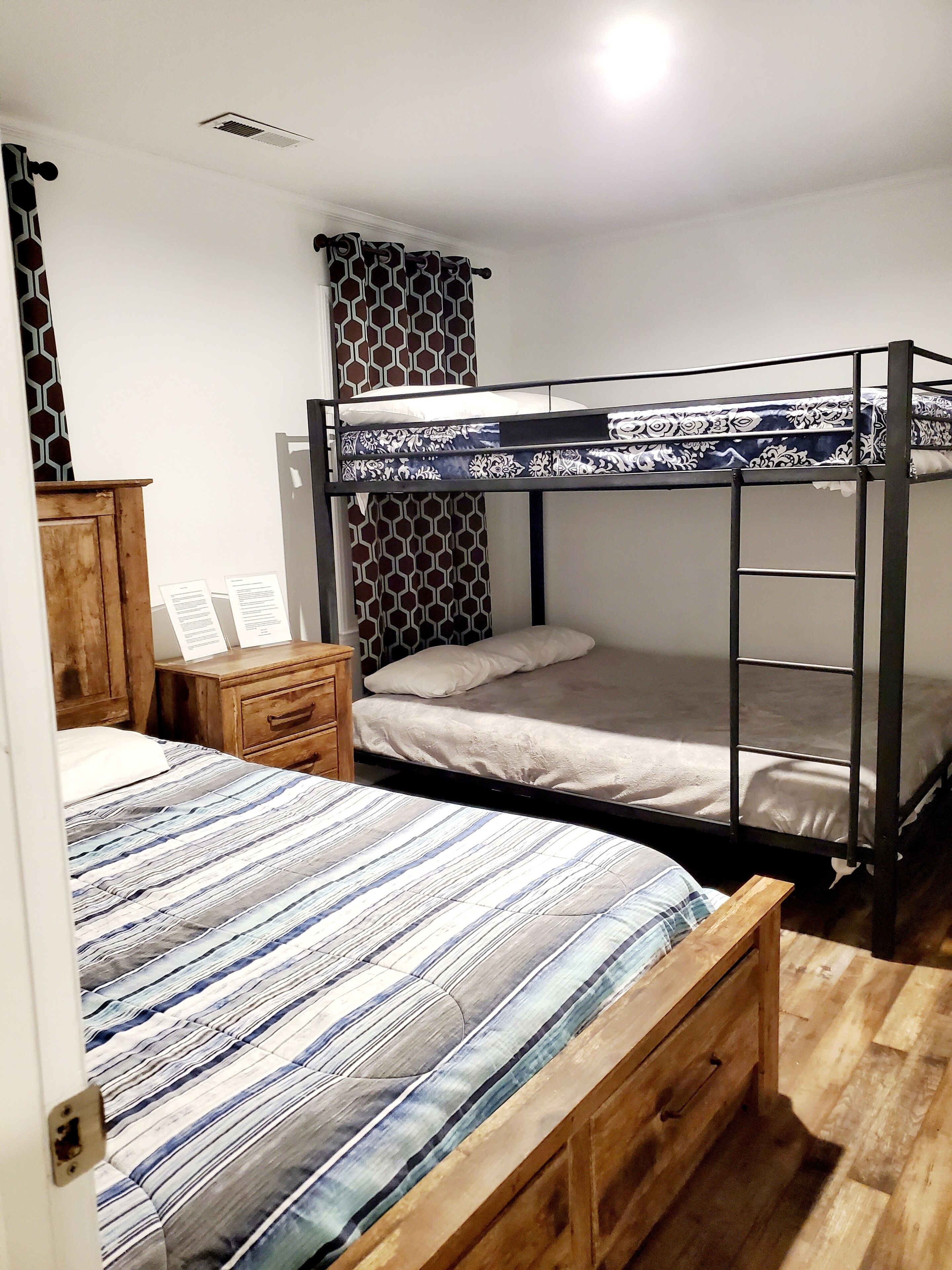 A room with bunk beds, a wooden dresser, and a desk with papers.