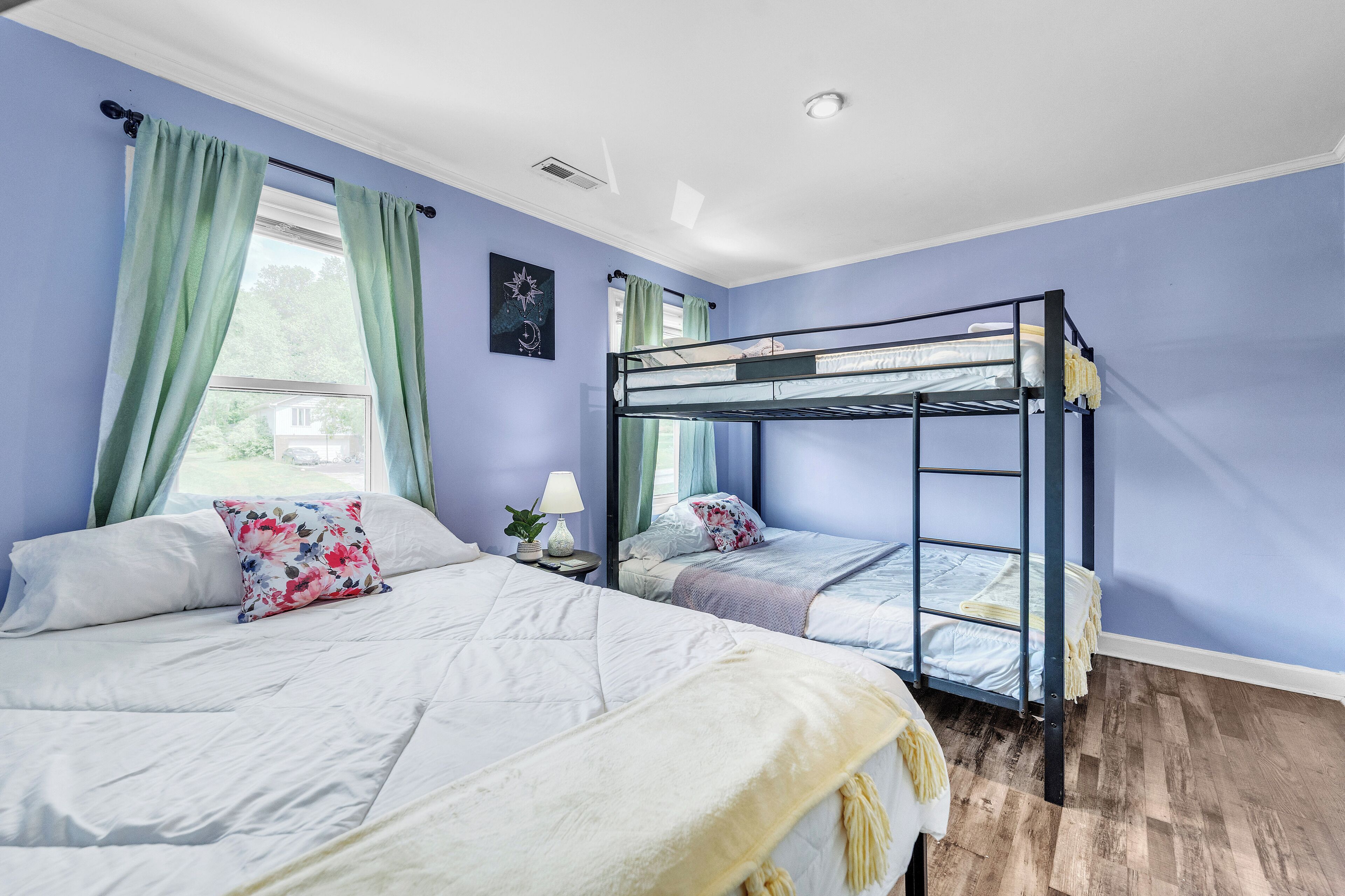 Una habitación con dos camas, una de ellas litera, y un ventanal con cortinas.