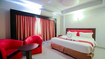 A hotel room with a bed, red armchair, and a small table.