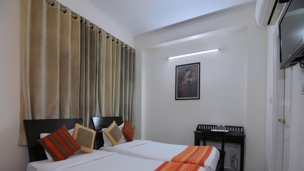 A hotel room with two beds, a desk, and a TV. - Mehra Residency at the Airport (New Delhi)