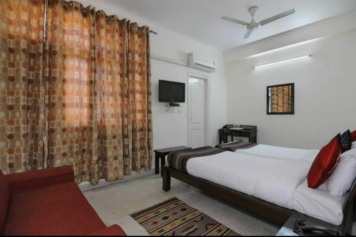 A hotel room with a bed, a TV, a ceiling fan, and a window with curtains.