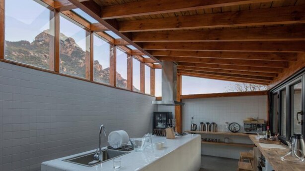 A modern kitchen with a large window, wooden ceiling beams, and a white countertop. - Yi She Mountain Inn (Changping)