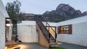 A modern building with a staircase leading to a wooden deck, surrounded by white brick walls and a mountainous backdrop. - Yi She Mountain Inn (Changping)
