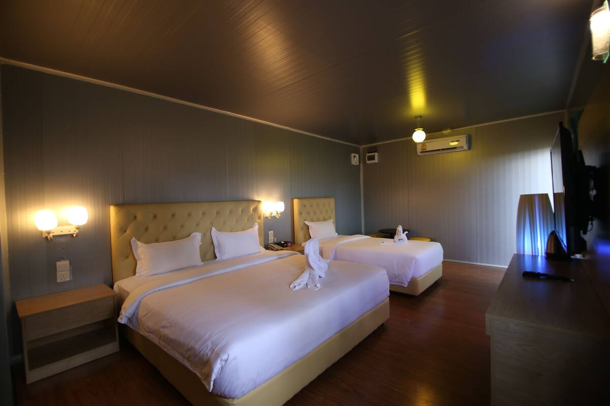 A hotel room with two beds, a wooden nightstand, a wall-mounted air conditioner, and a ceiling light fixture.