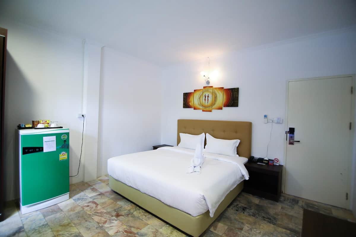 A hotel room with a bed, a green minibar, a wall-mounted artwork, and a door.