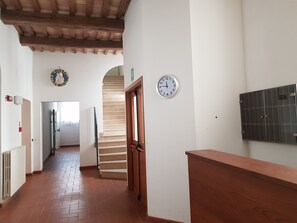 A hallway with a wooden ceiling, a staircase, a clock, and a door. - Domus Ecclesiae (Nocera Umbra)