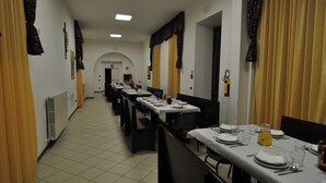 Un comedor amplio con mesas dispuestas para comidas, cortinas amarillas y suelo de baldosas.