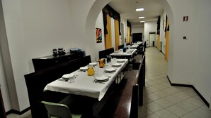 Un amplio comedor con varias mesas dispuestas para el servicio, paredes blancas y suelo de baldosas.