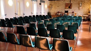 Un salón de conferencias con filas de sillas, una mesa de madera y una pared de piedra con un cuadro.