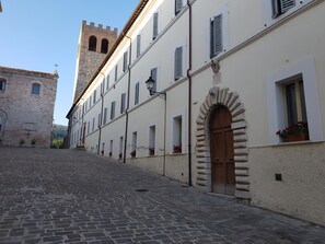 A cobblestone street with historic buildings, a tower, and a stone archway.