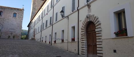 A cobblestone street with a building featuring a stone tower, arched windows, and a wooden door.