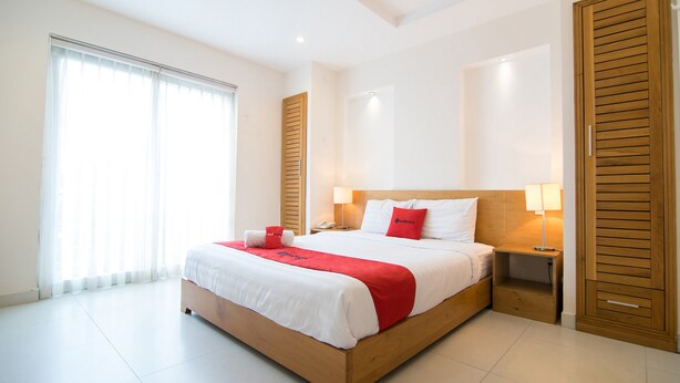 A spacious bedroom with a large bed, wooden headboard, bedside tables with lamps, and a sliding wooden door. - RedDoorz Plus near SECC D7 (Ho Chi Minh City)