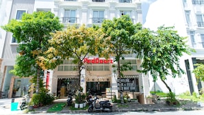 A hotel with a sign reading "BedDoornz" and a storefront with a sign in a foreign language. There are potted plants and a scooter parked in front. - RedDoorz Plus near SECC D7 (Ho Chi Minh City)