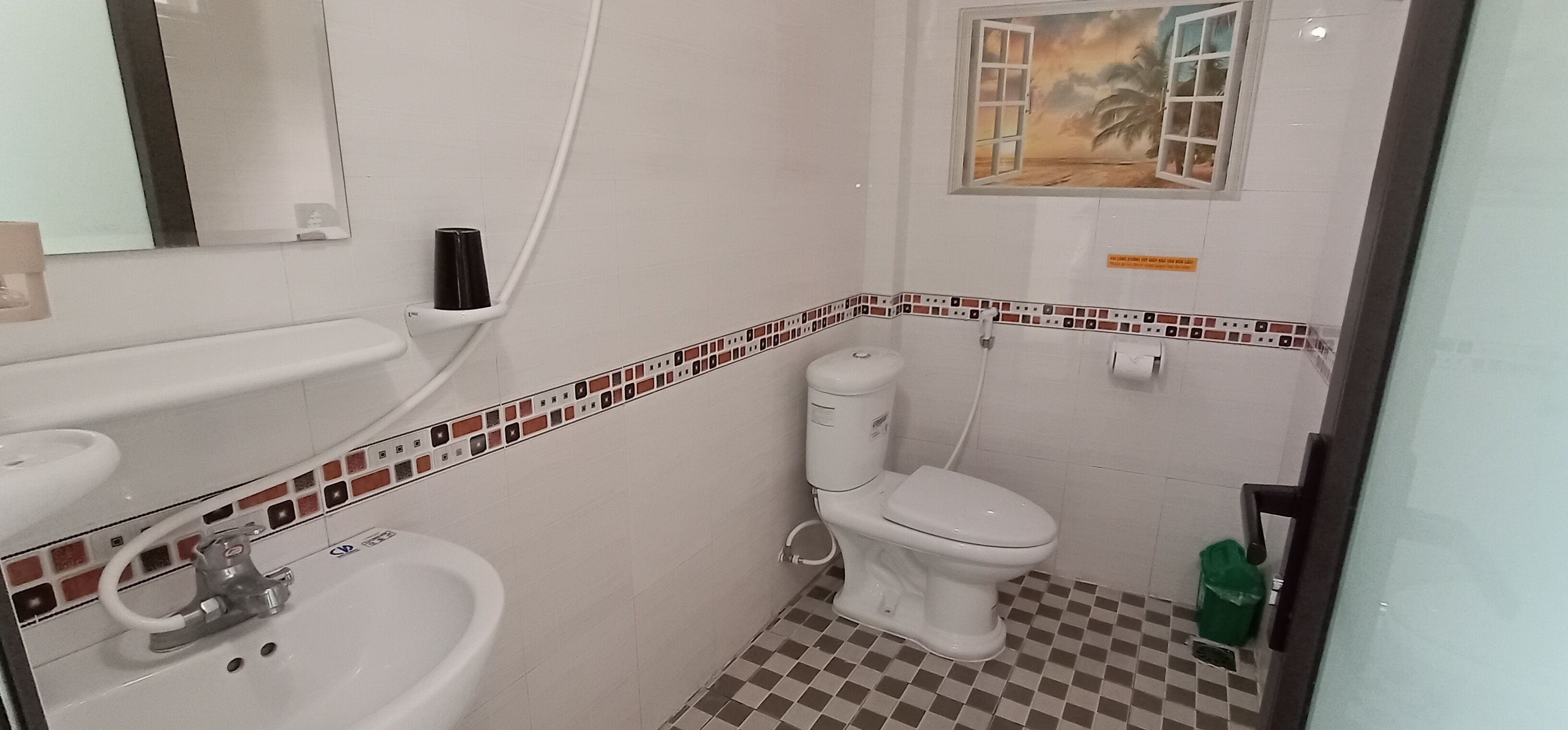 A bathroom with a sink, toilet, and a window with a view of palm trees.
