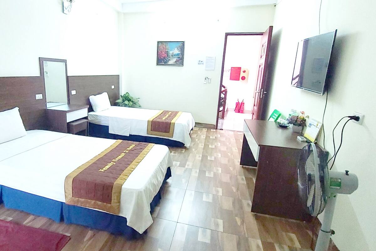 A hotel room with two beds, a desk, a chair, a TV, and a fan.